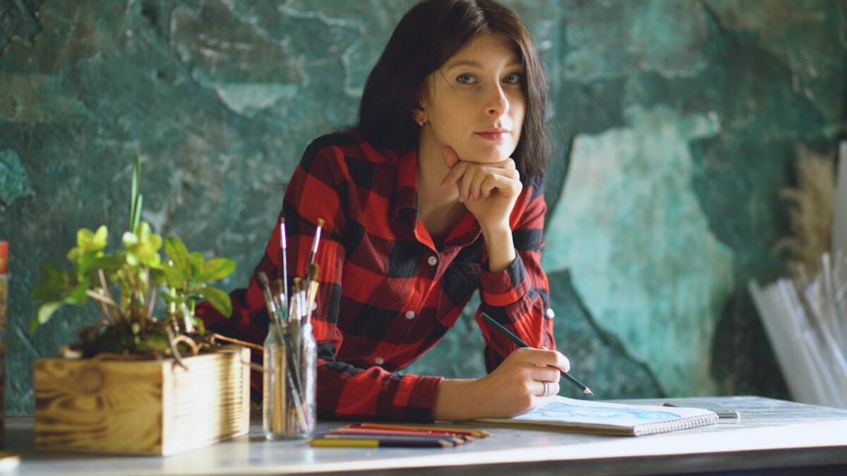 services-02 A young woman in a checkered shirt sketching in a vibrant art studio.