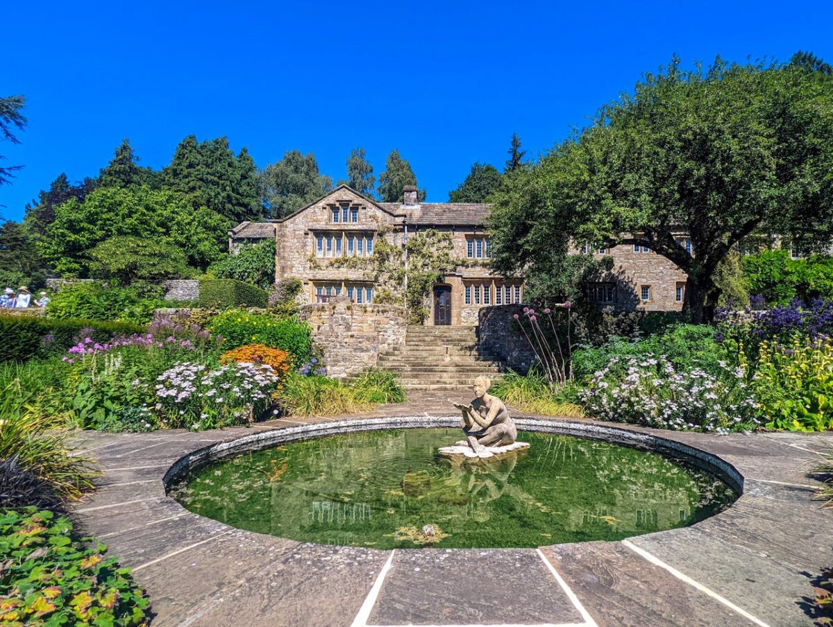 gallery-04 Serene scene of a beautiful English country garden with an ornamental pond and historic stone house.