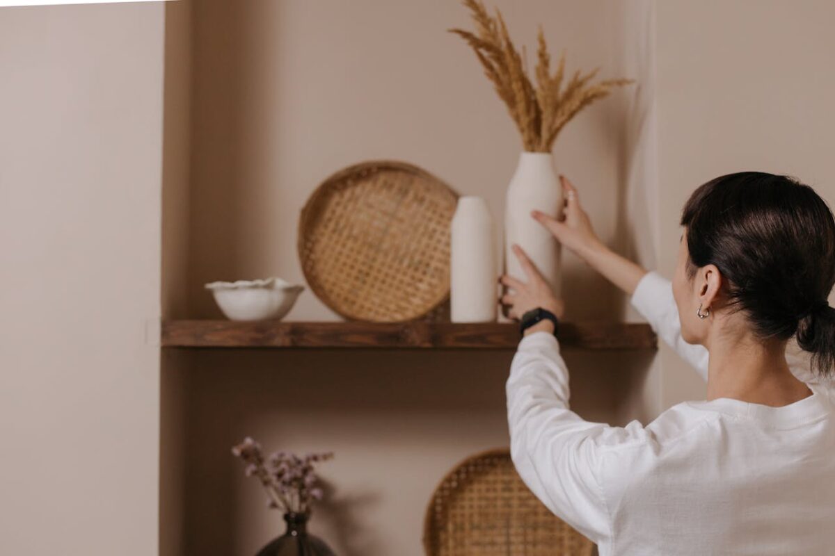 our-story A woman arranging vases on a rustic shelf, highlighting minimalist interior design.